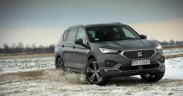 Szary Seat Tarraco SUV przemierza błotniste, zaśnieżone pole, wzbijając chmury brudu.
