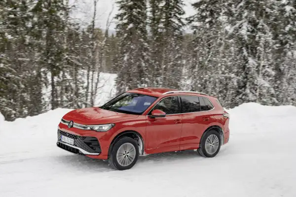 Czerwony Volkswagen Tiguan 5N pokonuje zasypaną śniegiem drogę w lesie.
