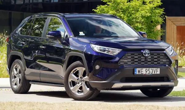 Elegancka, granatowa Toyota RAV4 5 generacji z przyciemnianymi szybami i chromowanymi felgami, zaparkowana na tle zieleni i nowoczesnego budynku.