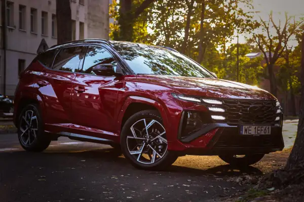 Czerwony Hyundai Tucson 4 w sportowej wersji N Line zaparkowany na tle jesiennych drzew i kamienicy.