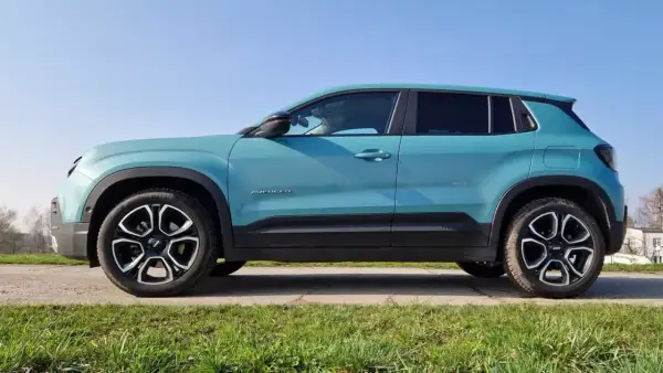 Turkusowy suv premium Jeep Avenger z czarnymi akcentami i felgami stoi na tle błękitnego nieba.